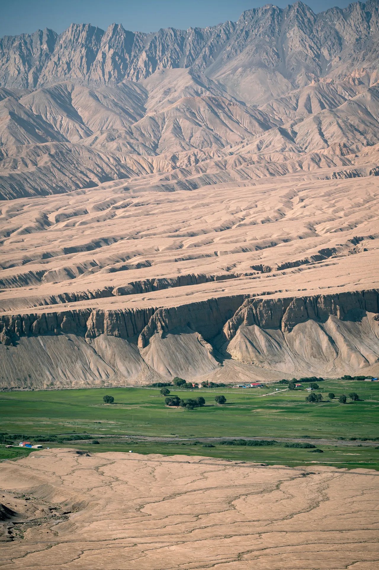 Green fields below layered, arid mountain ridges